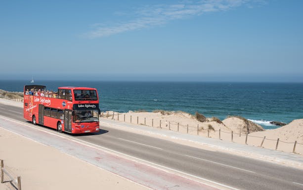 Lisbon sightseeing bus on coastal road with ocean view.