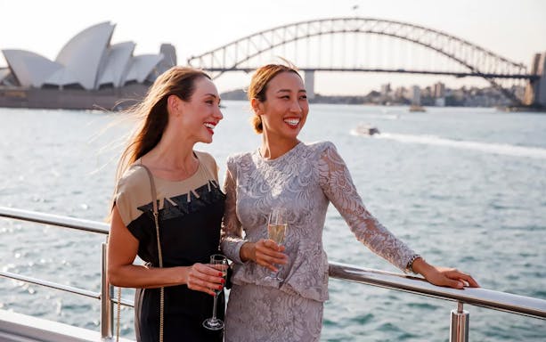 Two people enjoying champagne on a boat with Sydney Opera House and Harbour Bridge in the background.