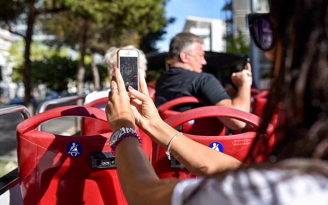 Open-top bus tour in Lisbon with passengers taking photos.