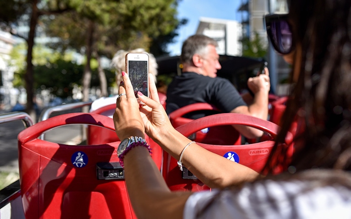 Open-top bus tour in Lisbon with passengers taking photos.