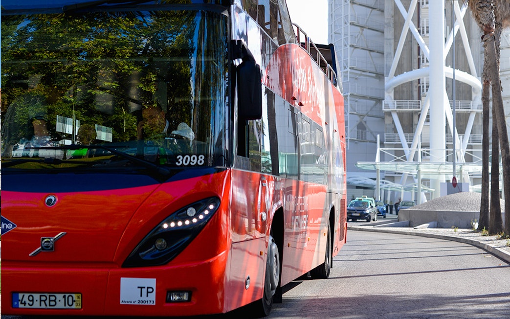Red double-decker bus on Lisbon street near modern architecture, part of hop-on-hop-off tour.