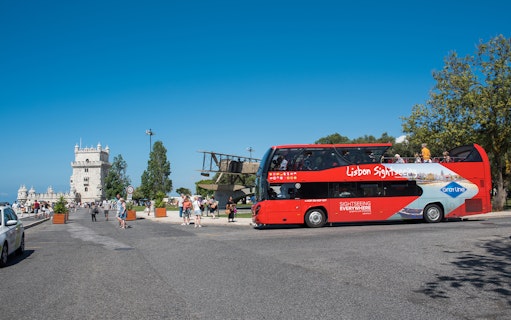 Red sightseeing bus near Belém Tower on Lisbon hop-on-hop-off tour.