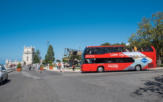Red sightseeing bus near Belém Tower on Lisbon hop-on-hop-off tour.