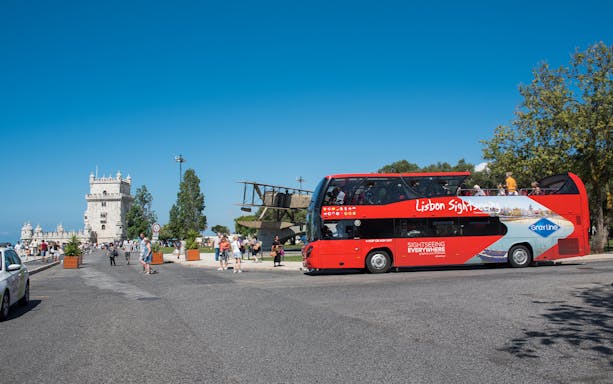 Red sightseeing bus near Belém Tower on Lisbon hop-on-hop-off tour.