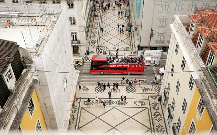 Lisbon sightseeing bus on patterned street during hop-on-hop-off tour.