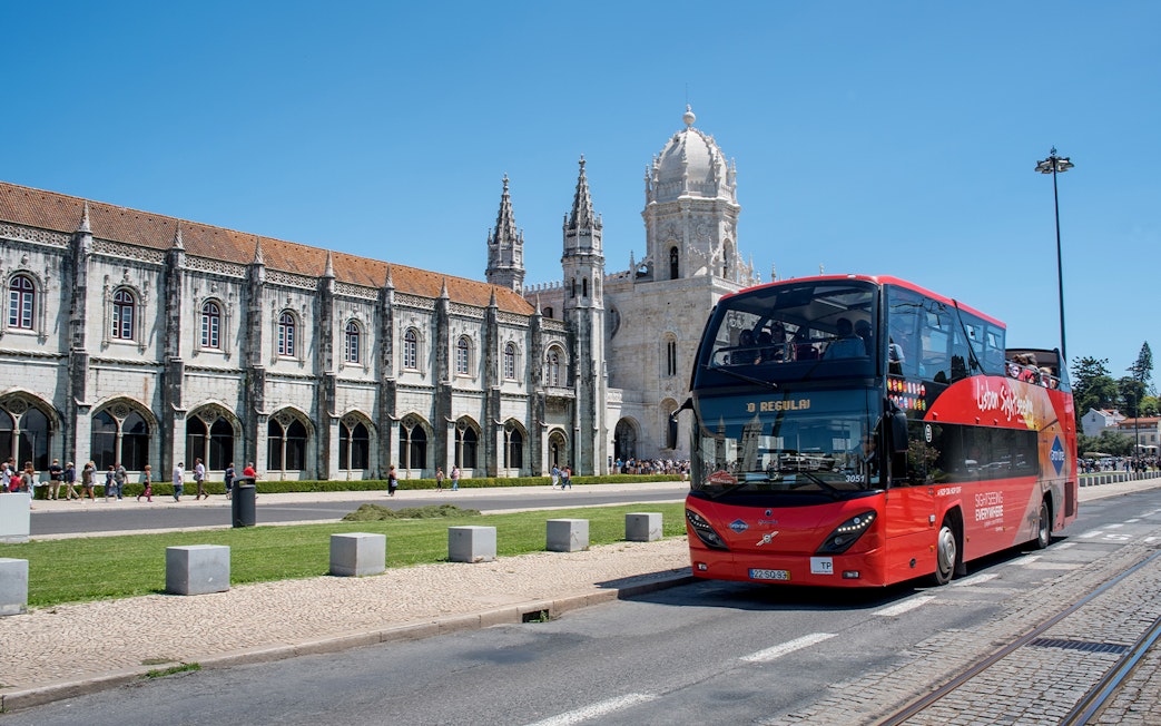 Red double-decker bus in front of Jerónimos Monastery, Lisbon, on a hop-on-hop-off tour.