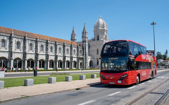 Red double-decker bus in front of Jerónimos Monastery, Lisbon, on a hop-on-hop-off tour.