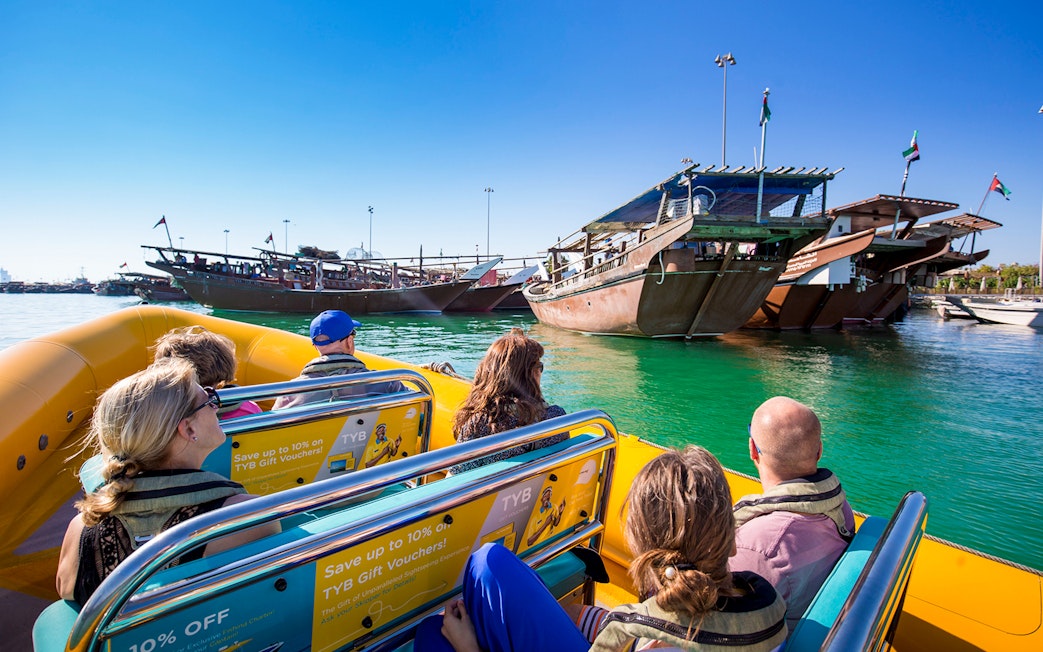 Sightseers on a yellow speedboat tour in Abu Dhabi, passing traditional wooden boats.