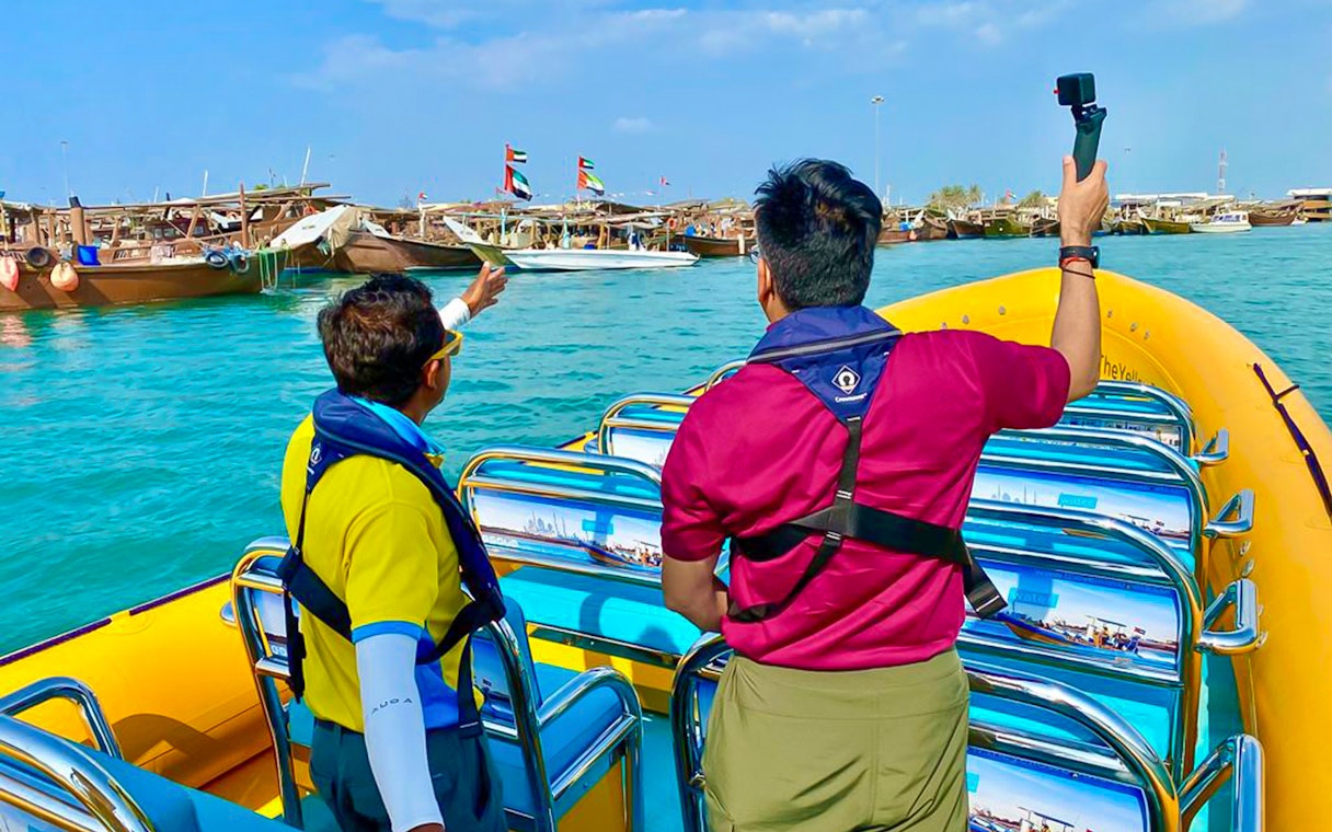 Tourists on a yellow speedboat in Abu Dhabi, viewing traditional boats in the harbor.