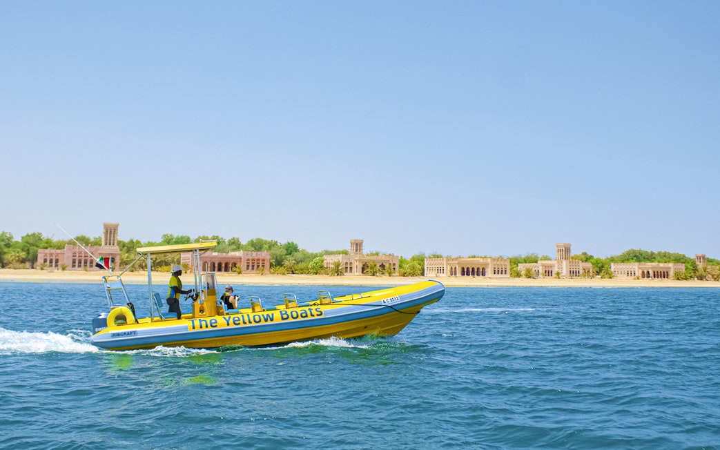 Yellow speedboat touring Yas Island with historic buildings in the background.