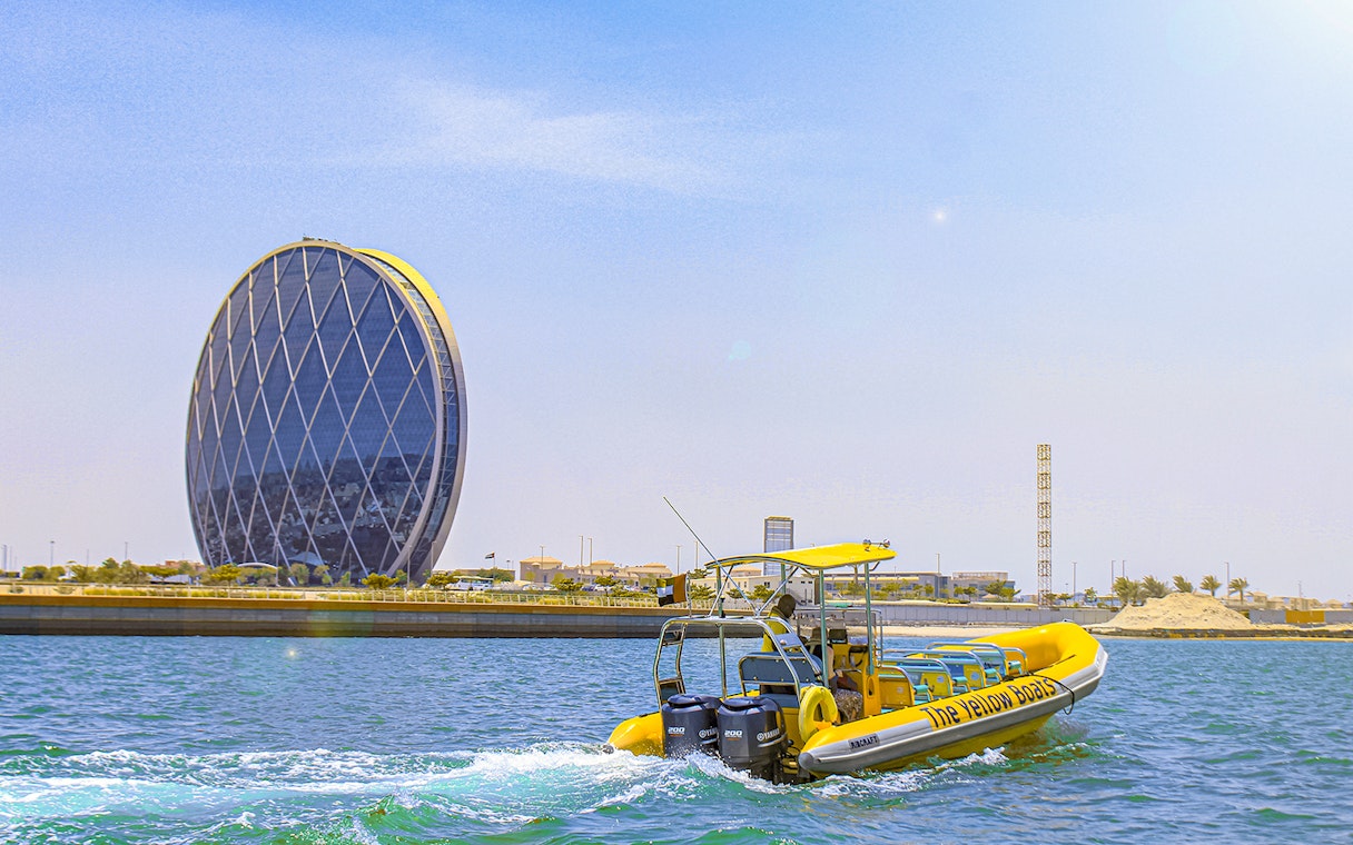 Yellow speedboat touring Yas Island with Aldar HQ building in the background.
