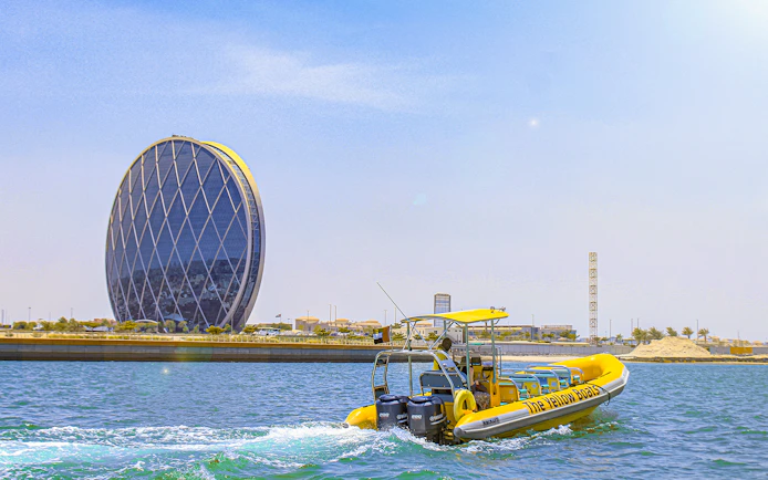 Yellow speedboat touring Yas Island with Aldar HQ building in the background.
