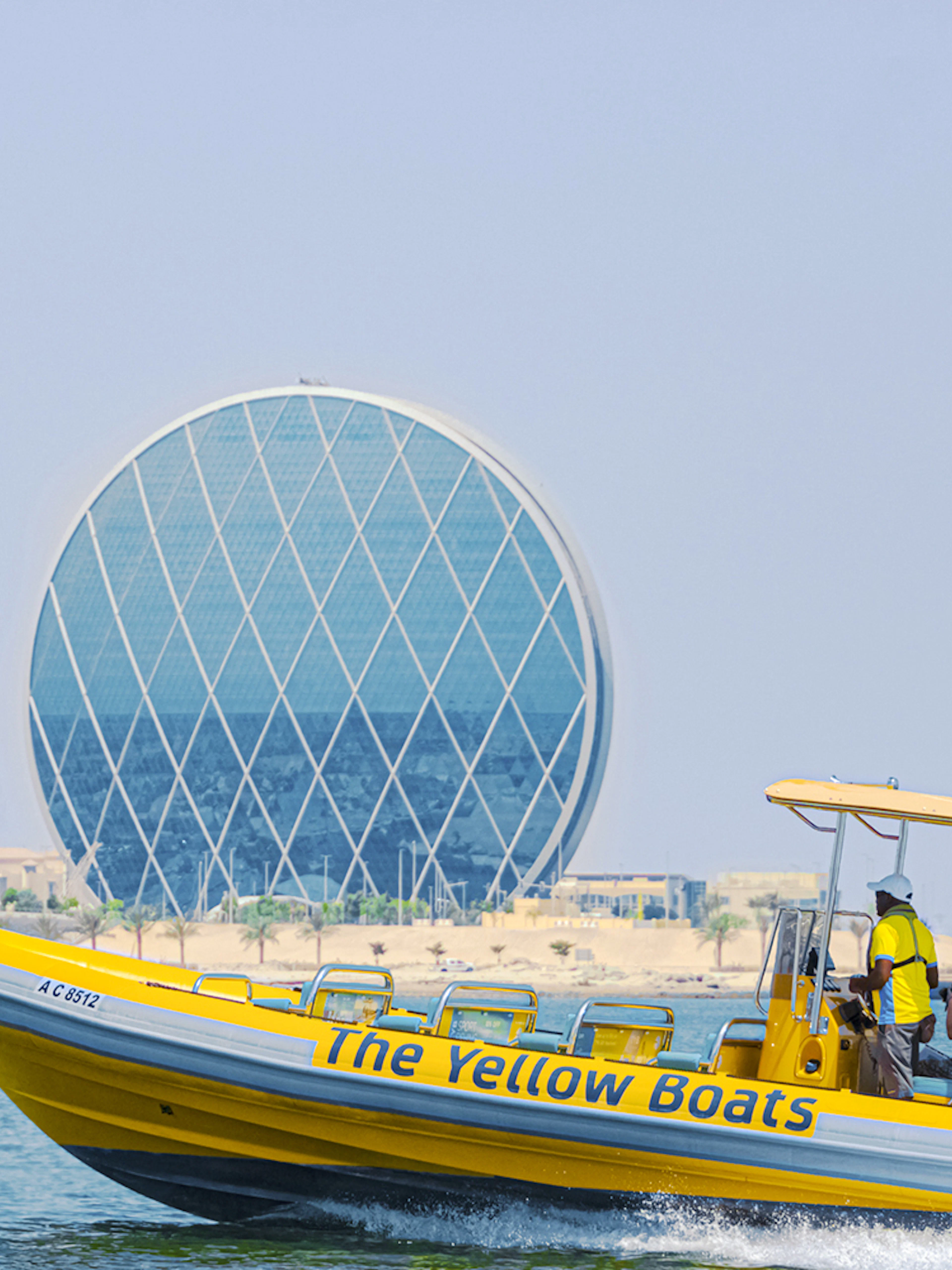 Yellow speedboat touring Yas Island with Aldar HQ building in the background.