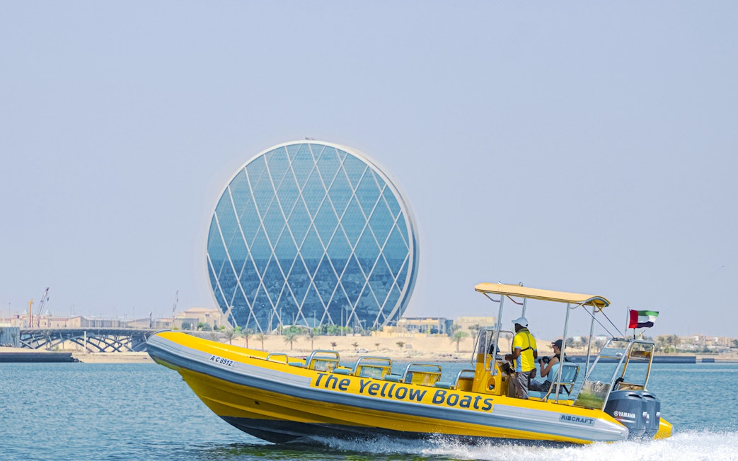 Yellow speedboat touring Yas Island with Aldar HQ building in the background.