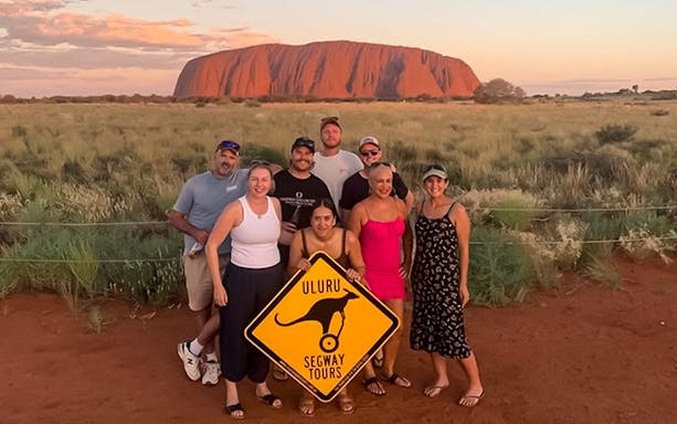 Group posing with Uluru Segway Tours sign in front of Uluru, Australia.