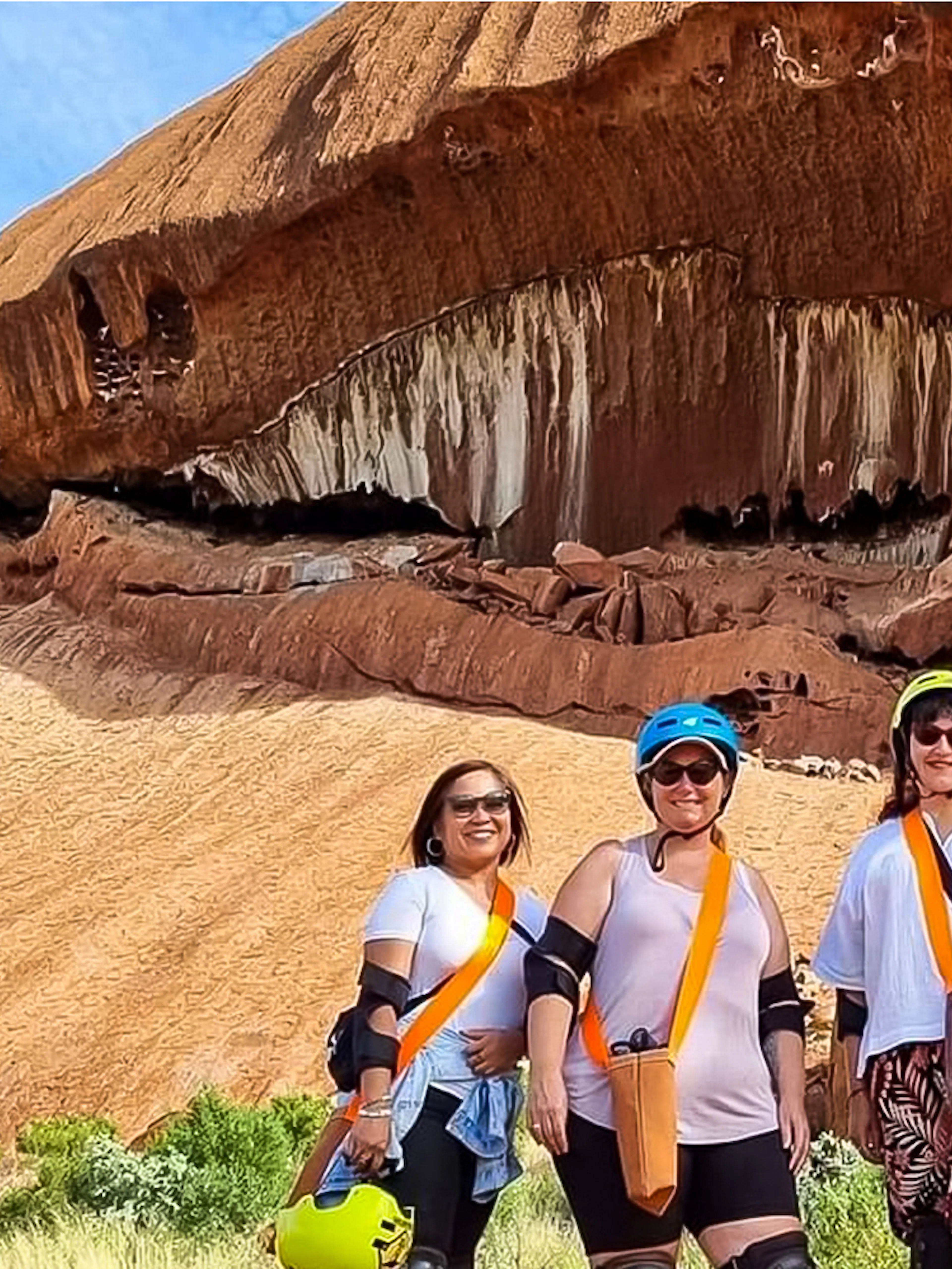 Visitors in helmets and gear standing in front of Uluru rock formation during a Segway tour.