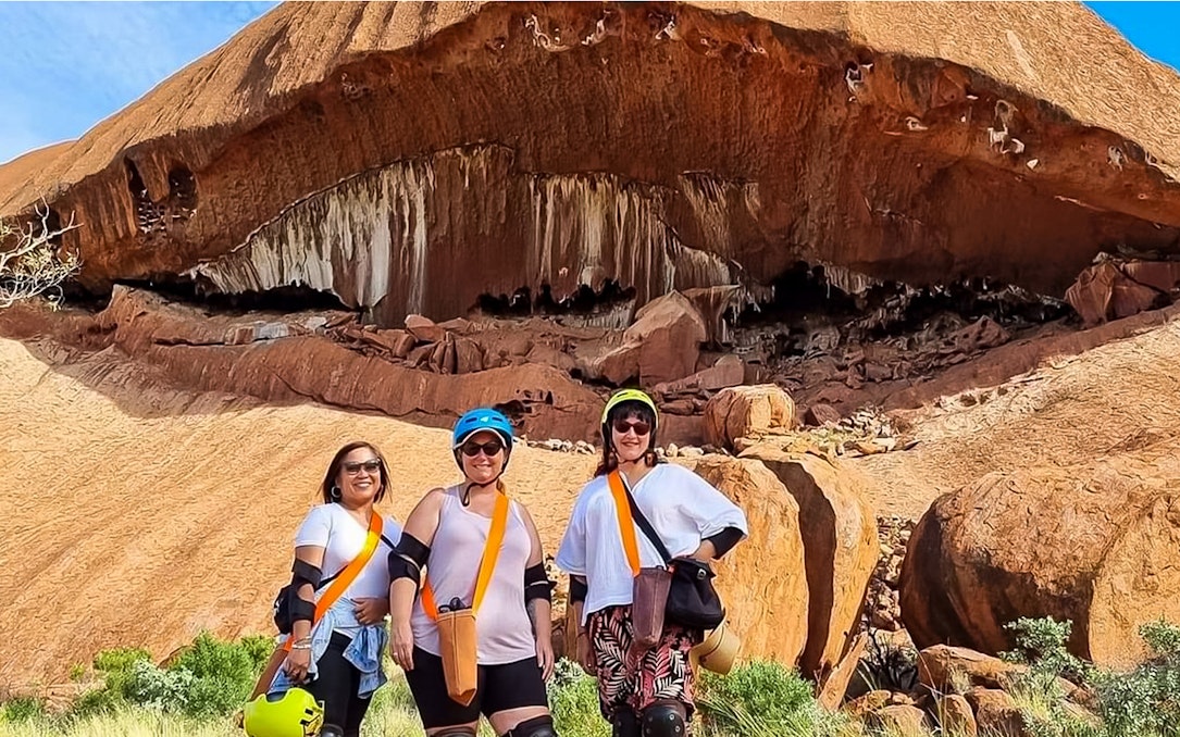 Visitors in helmets and gear standing in front of Uluru rock formation during a Segway tour.