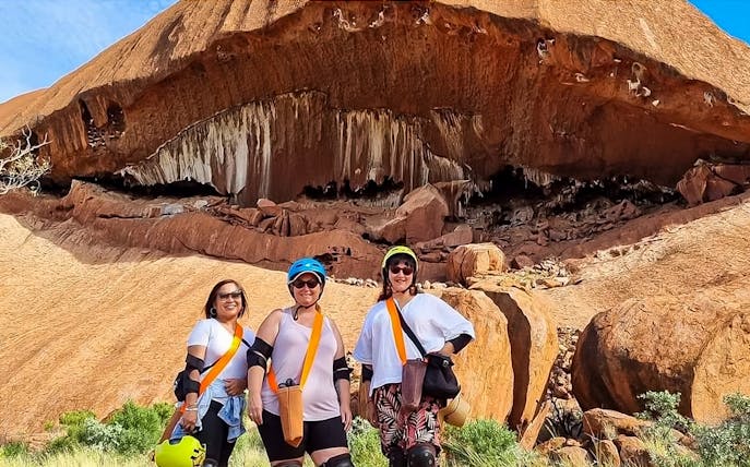 Visitors in helmets and gear standing in front of Uluru rock formation during a Segway tour.