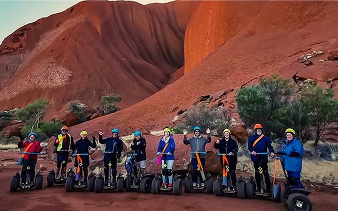 Group on Segways touring Uluru, Australia, with red rock formations in the background.