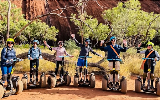 Group on Segways exploring Uluru with red rock and trees in the background.