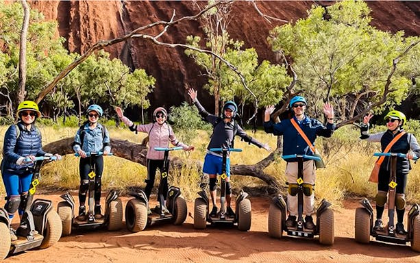 Group on Segways exploring Uluru with red rock and trees in the background.