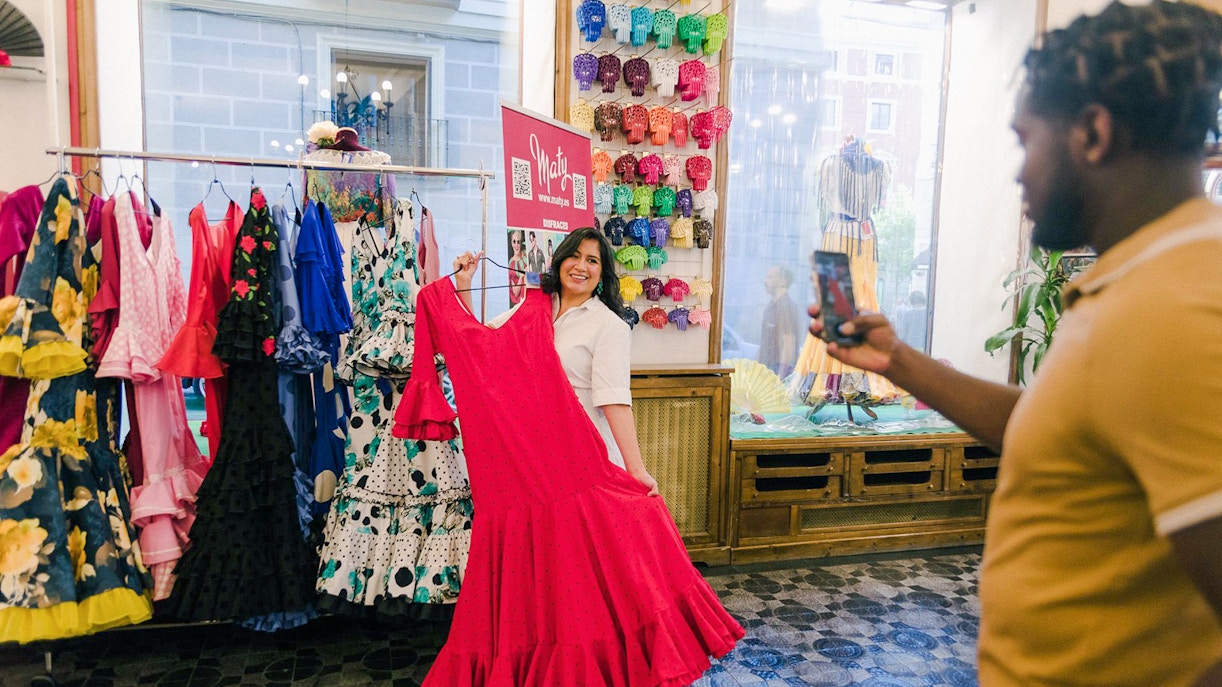 Woman holding a red flamenco dress in a Madrid shop during a guided walking tour.
