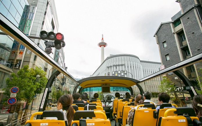 Open-top bus tour in Kyoto passing Kyoto Tower and city buildings.