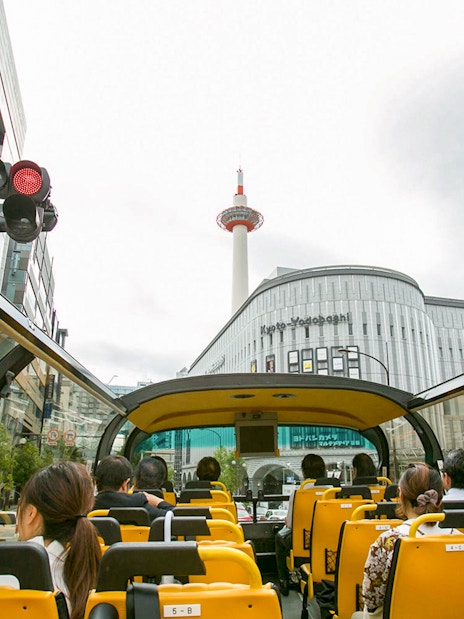 Open-top bus tour in Kyoto passing Kyoto Tower and city buildings.