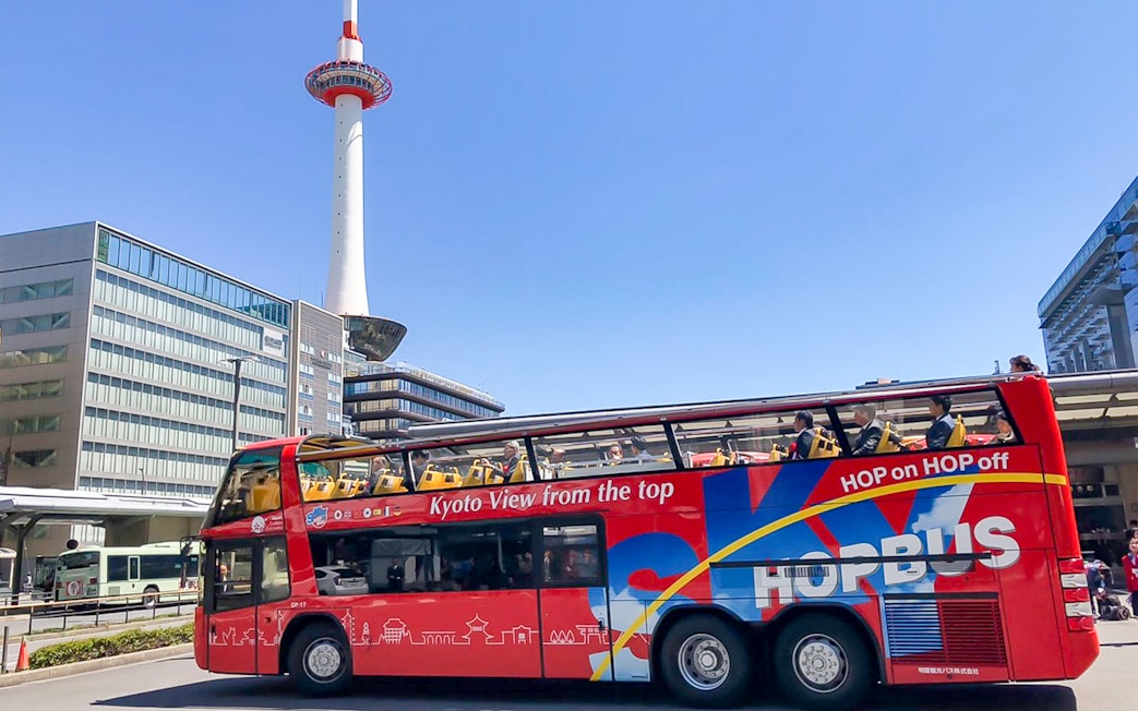 Kyoto Sky Hop Bus passing Kyoto Tower on a clear day.