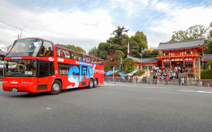 Kyoto sightseeing bus passing by Yasaka Shrine with tourists on board.
