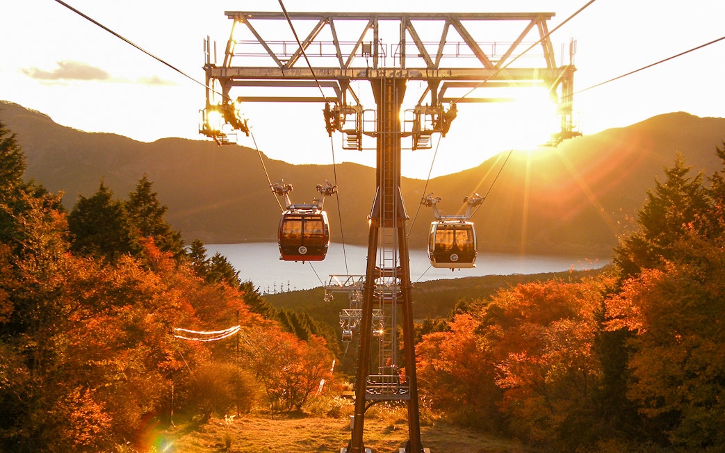 Cable cars over autumn foliage in Hakone with a view of the lake and mountains.