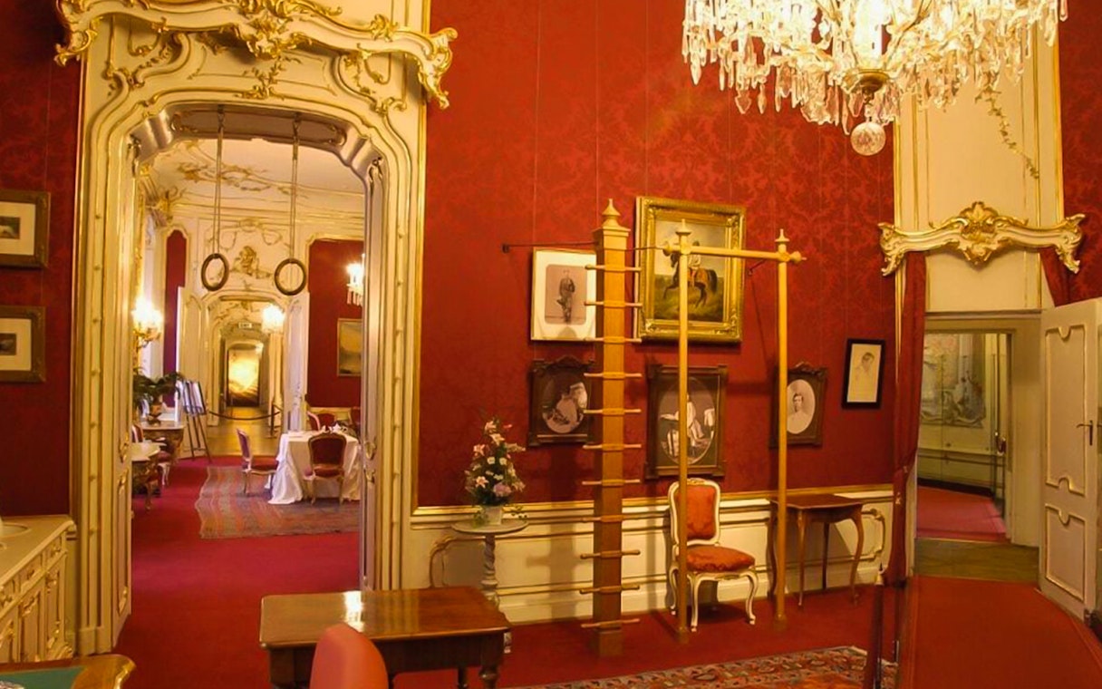 Empress Sisi's Vienna tour, ornate red room with chandeliers and historical portraits.