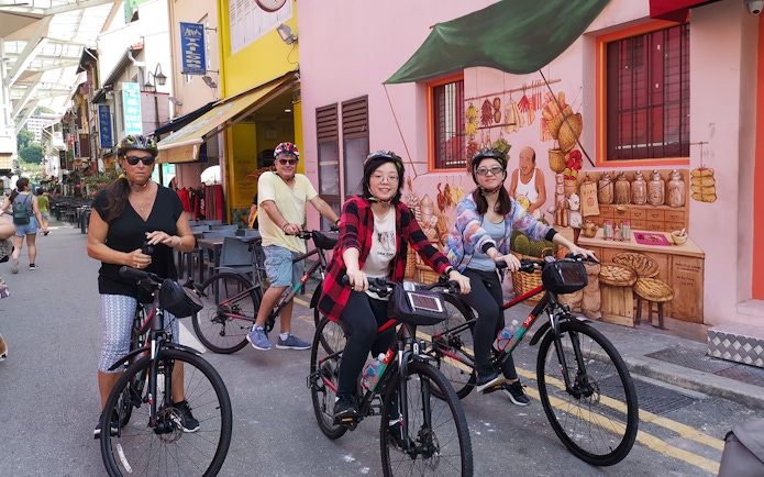 Cyclists exploring a vibrant street in Singapore with colorful murals and local shops.