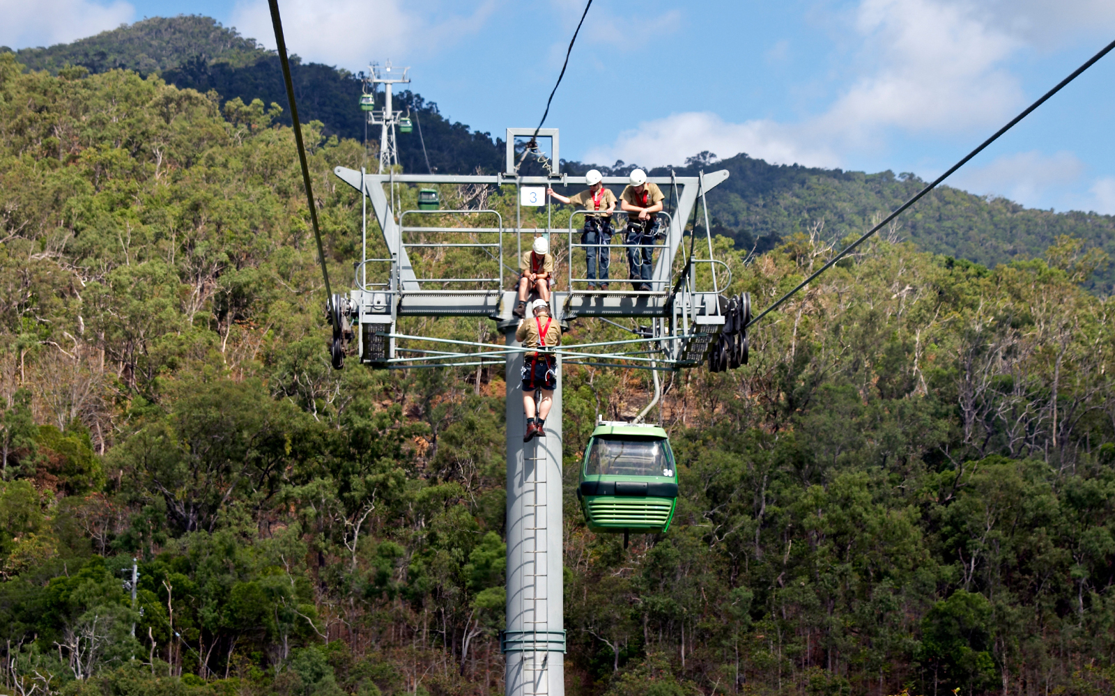 Skyrail gondola over lush forest near Cairns, Australia, with maintenance workers on the tower.
