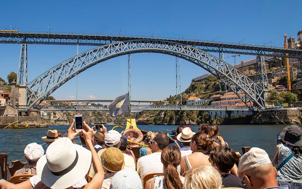 Tourists on a boat cruise under Dom Luís I Bridge in Porto, Portugal.