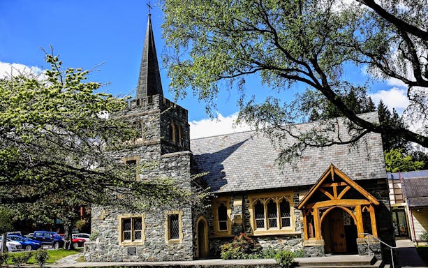 Stone church with steeple surrounded by trees in Queenstown, part of the Mt Cook & Lake Tekapo tour.
