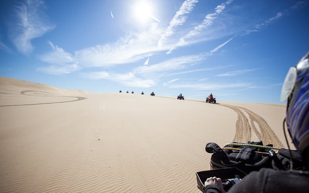 Quad bikes riding on sand dunes under a clear sky at Stockton Beach.