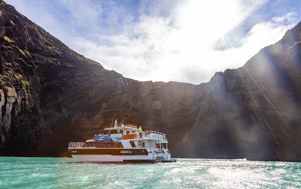 Cruise boat navigating turquoise waters near rocky cliffs in Akaroa.