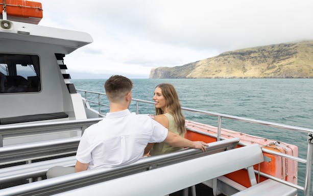 Couple enjoying a boat cruise with scenic views of Akaroa's coastline.