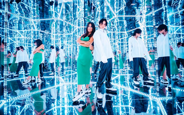 Visitors in a mirrored room at Studio of Wonders, surrounded by reflections and neon lights.