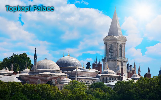Topkapi Palace in Istanbul with domes and tower under a blue sky.