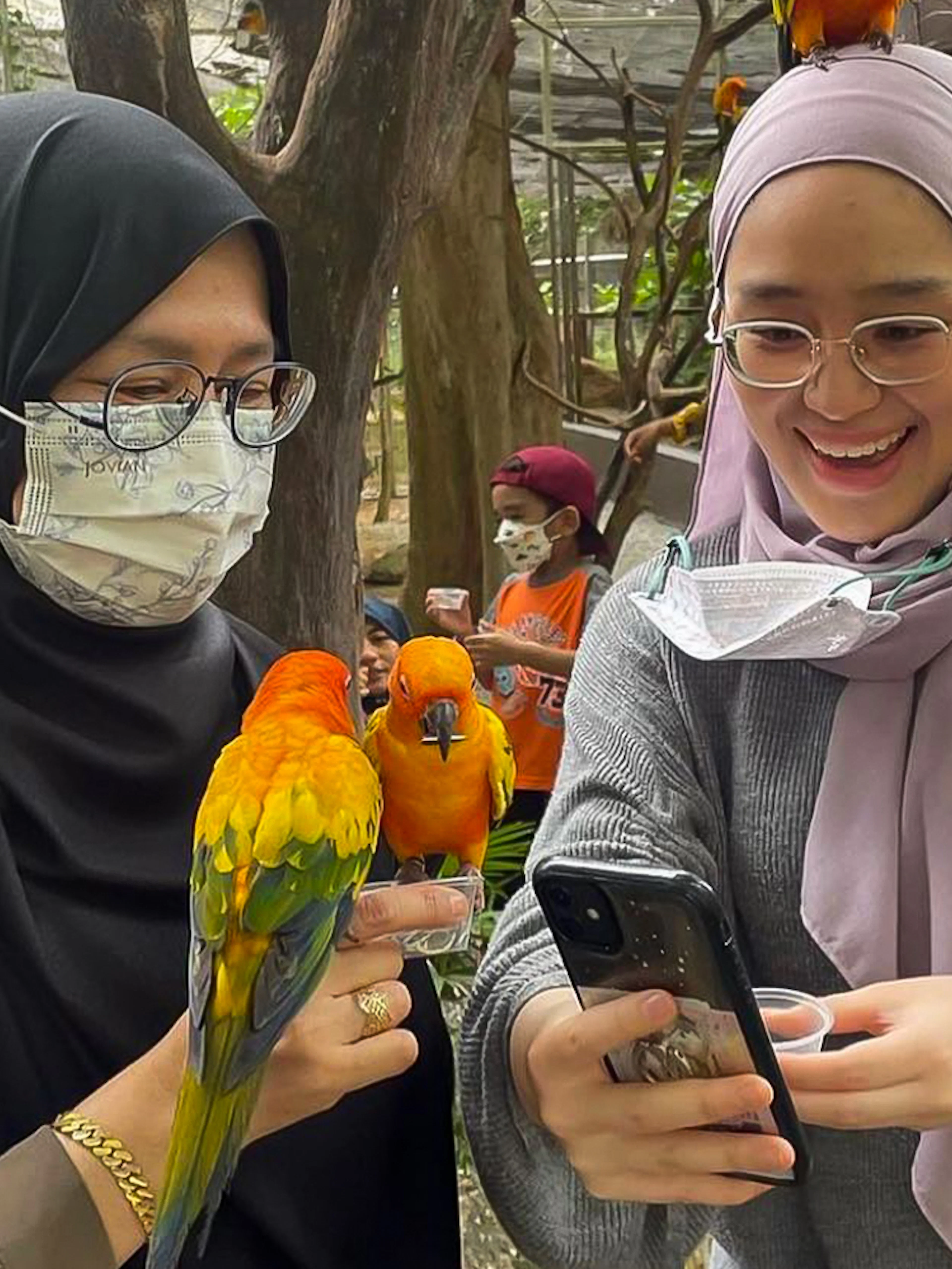 Visitors interacting with colorful parrots at Zoo Melaka, Malaysia.