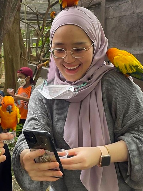 Visitors interacting with colorful parrots at Zoo Melaka, Malaysia.