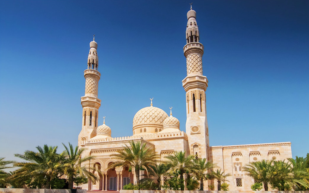 Jumeirah Mosque with palm trees under a clear blue sky in Dubai.