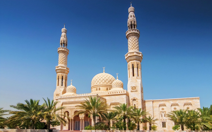 Jumeirah Mosque with palm trees under a clear blue sky in Dubai.
