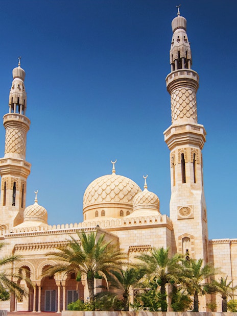 Jumeirah Mosque with palm trees under a clear blue sky in Dubai.