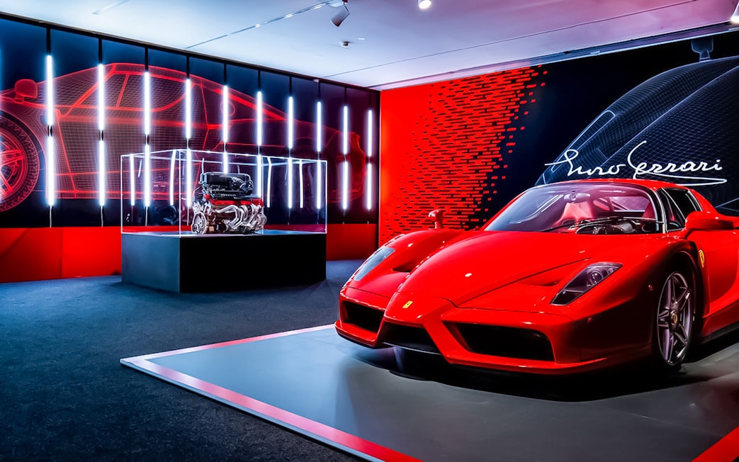 Red Ferrari Enzo displayed at Ferrari Museum Maranello with engine exhibit in background.