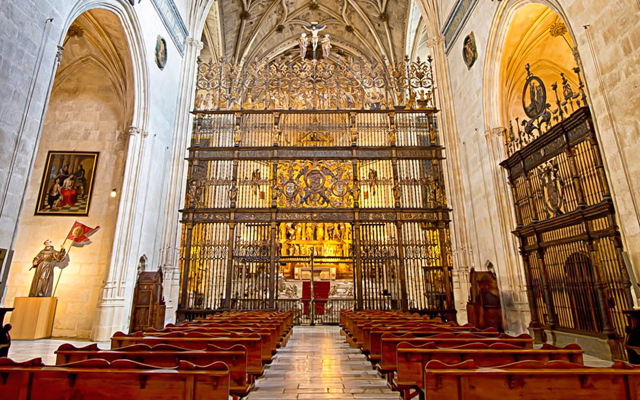 Interior of the Royal Chapel of Granada with ornate altar and wooden pews.