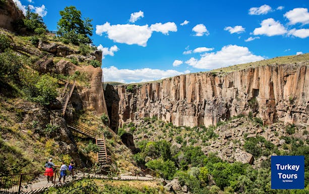 Visitors walking along a path in Ihlara Valley, Cappadocia, with steep cliffs and greenery.