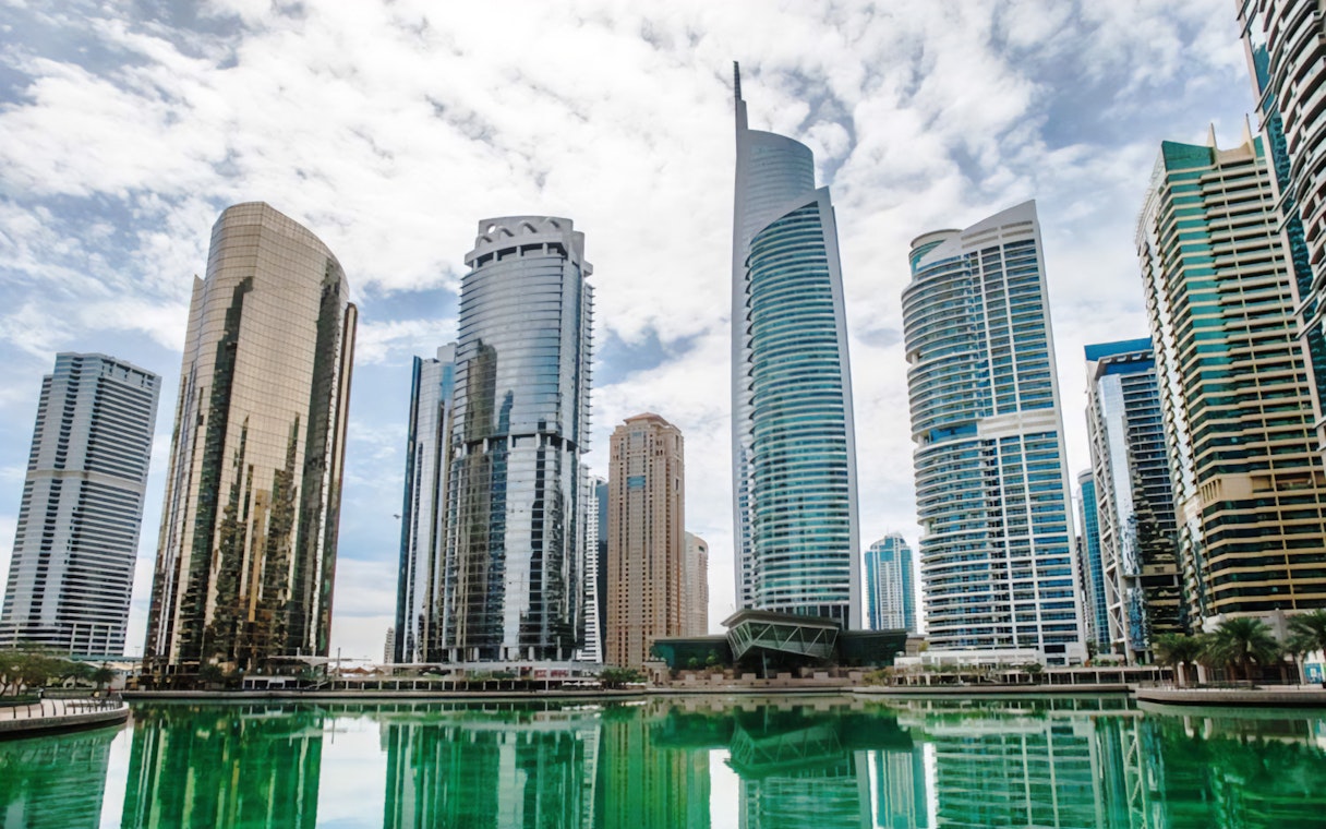Skyscrapers in Dubai's modern cityscape reflecting in a waterfront, part of guided tour.